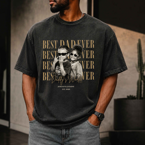 Man wearing a black t-shirt with a graphic of two children and text 'Best Dad Ever' in a room.